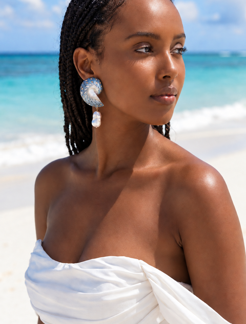 A model wears Medium Jaguar Nautilus Shell Drop Earrings with a white off-the-shoulder dress on the beach | Lily Frank Jewelry