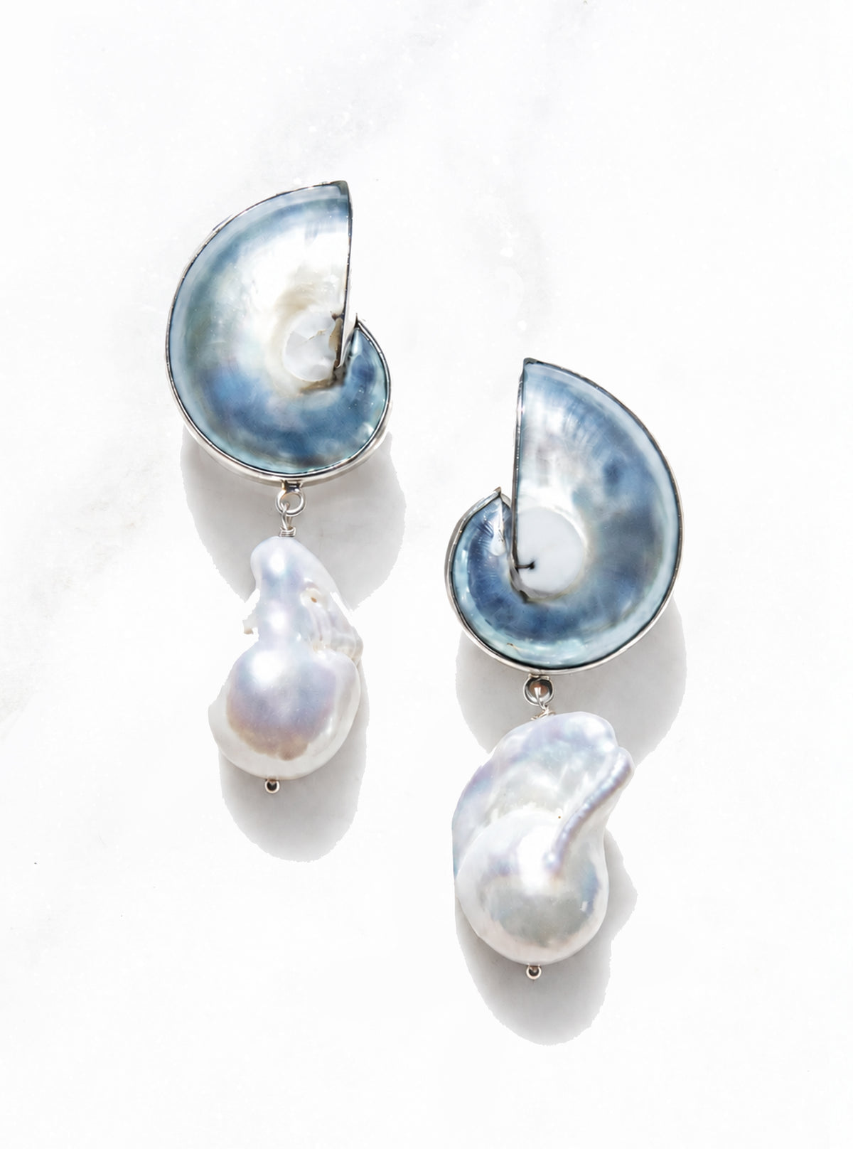 A pair of 925 silver encased blue nautilus earrings on a white marble background | Lily Frank Jewelry