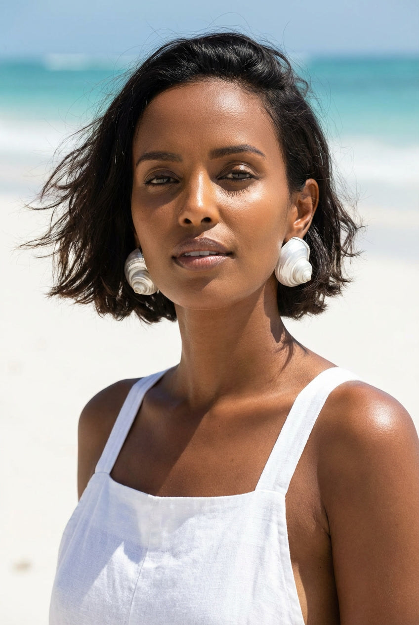 Woman wearing a pair of Betsy Turban Shell Earrings and a white top standing on a beach | Lily Frank Jewelry