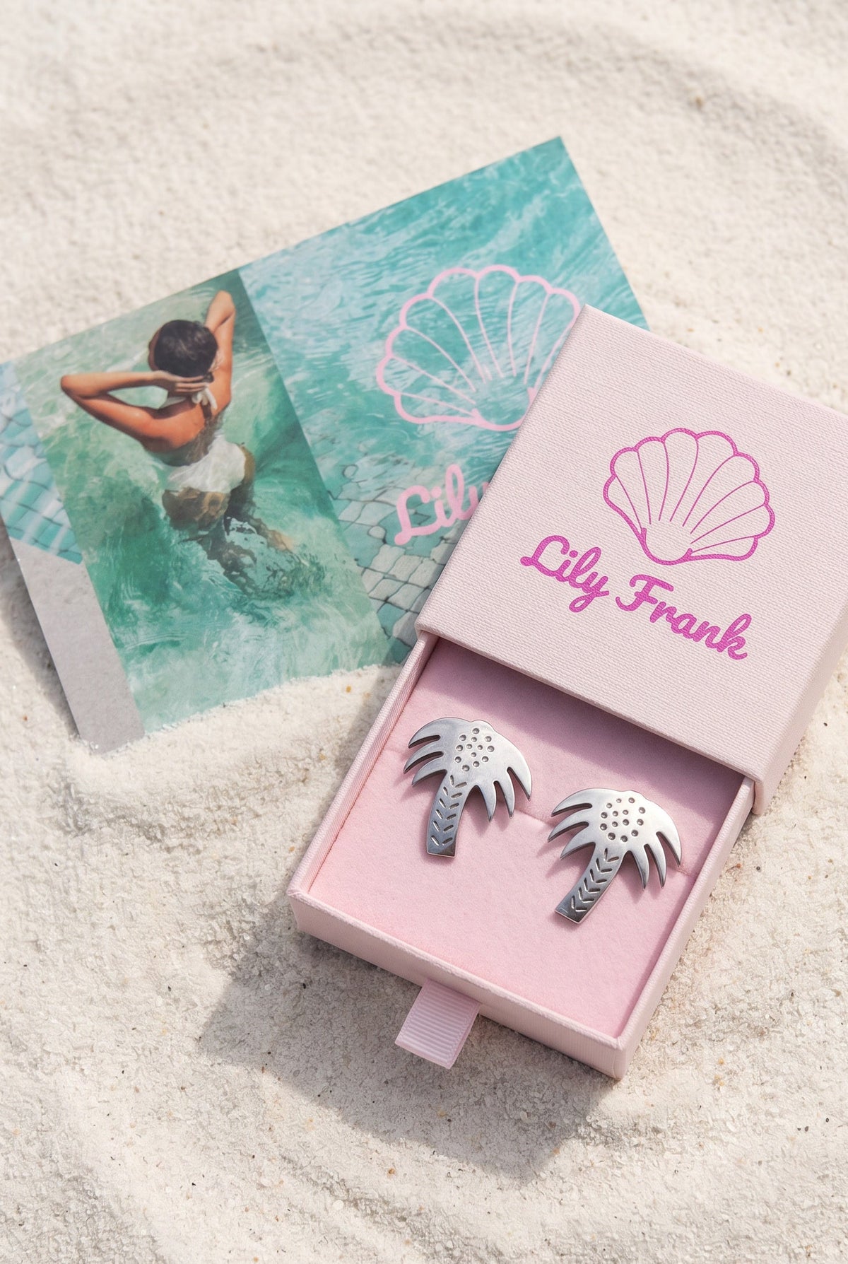 A pair of Vintage 925 Silver Palm Tree Earrings in a pink jewelry box on sand beside a turquoise brand card | Lily Frank Jewelry