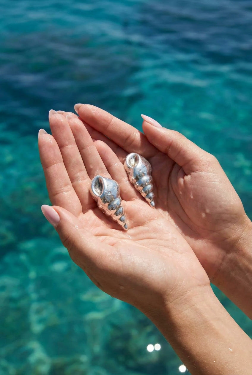 Vintage 925 silver trumpet shell earrings held in hands over ocean water — Lily Frank Jewelry