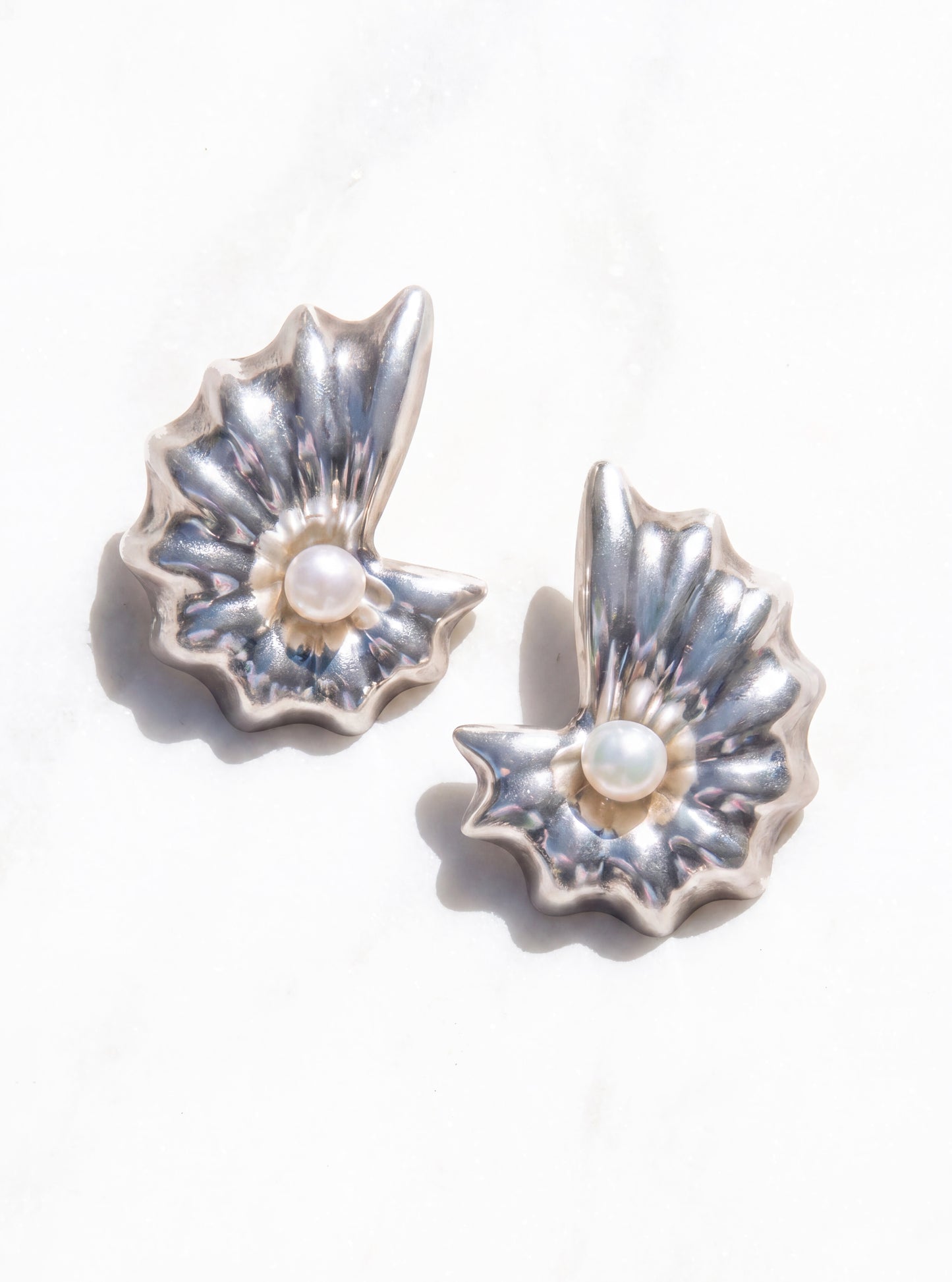 A pair of concha pearl shell earrings with textured petals and a small white pearl at the center, displayed on a light marble surface | Lily Frank Jewelry
