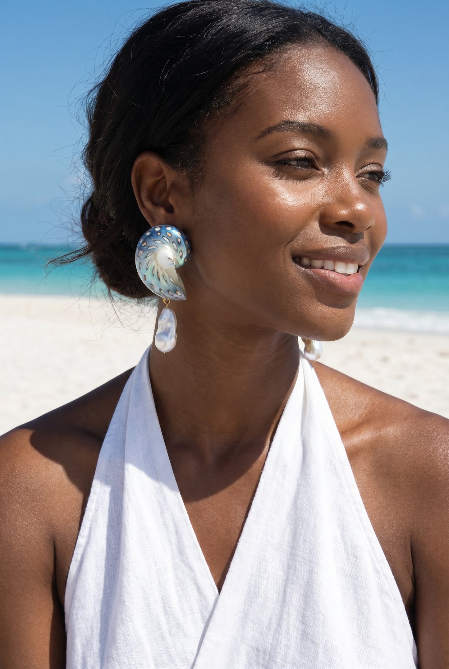 Woman on a beach wearing a white halter top and a pair Large Jaguar Nautilus Shell Drop Earrings | Lily Frank Jewelry