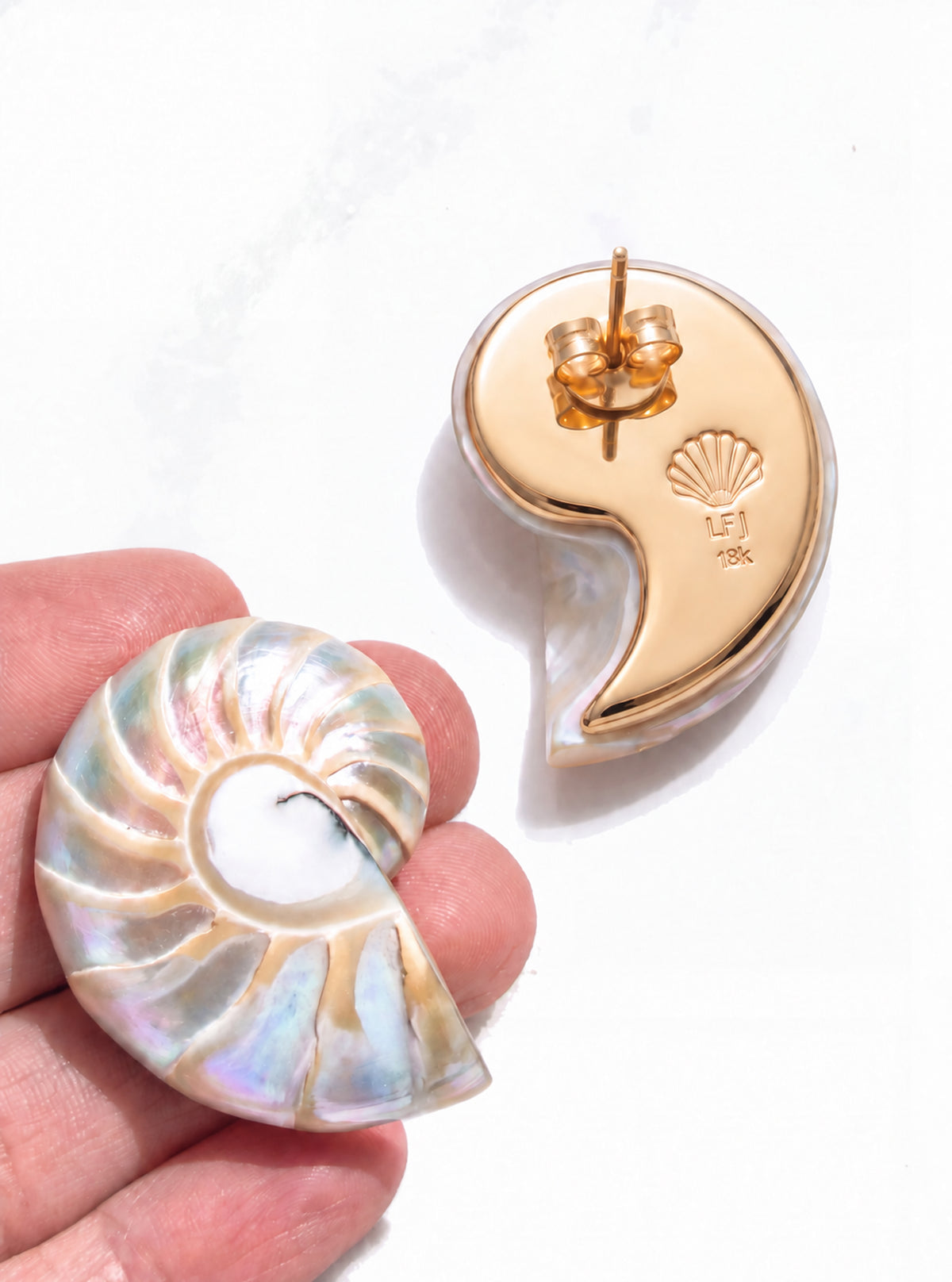 An overhead product shot of the large pearl nautilus shell earrings with 18k gold backplate on a white marble backdrop | Lily Frank Jewelry 