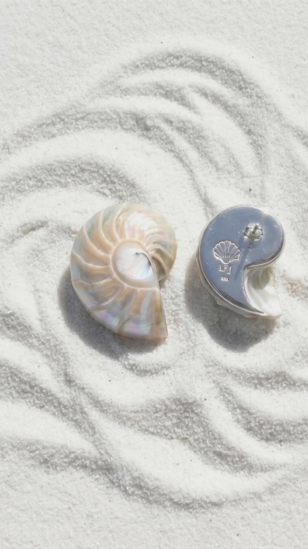 A pair of Small Pearl Nautilus Shell Earrings with 925 silver backplate lying on white sand at the beach | Lily Frank Jewelry