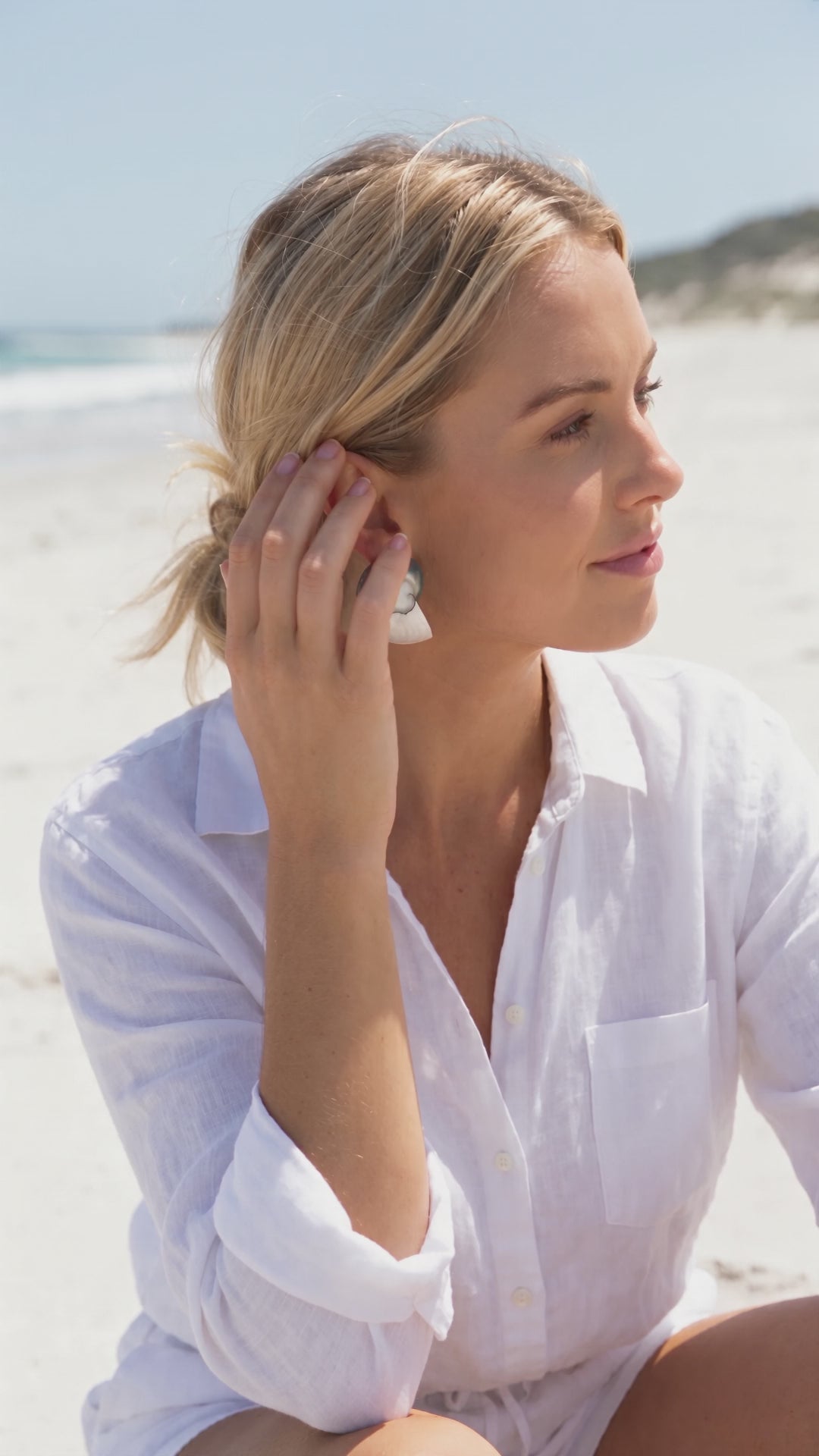 Model in a white shirt lowering her hand and turning toward the camera, wearing Large Two Toned Nautilus Shell Earrings | Lily Frank Jewelry