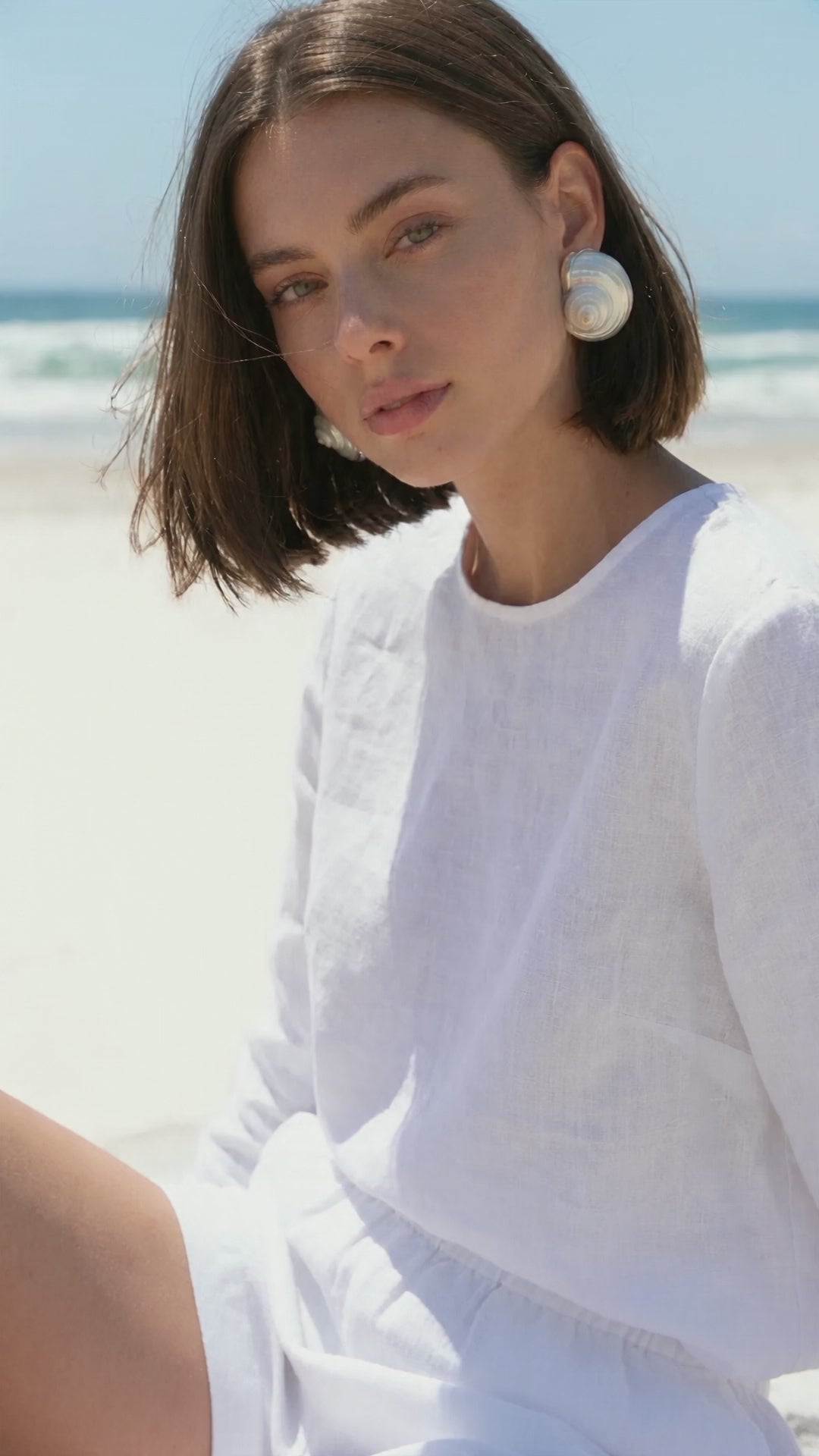 A woman sits on a beach wearing the Betsy Turban Shell Earrings | Lily Frank Jewelry