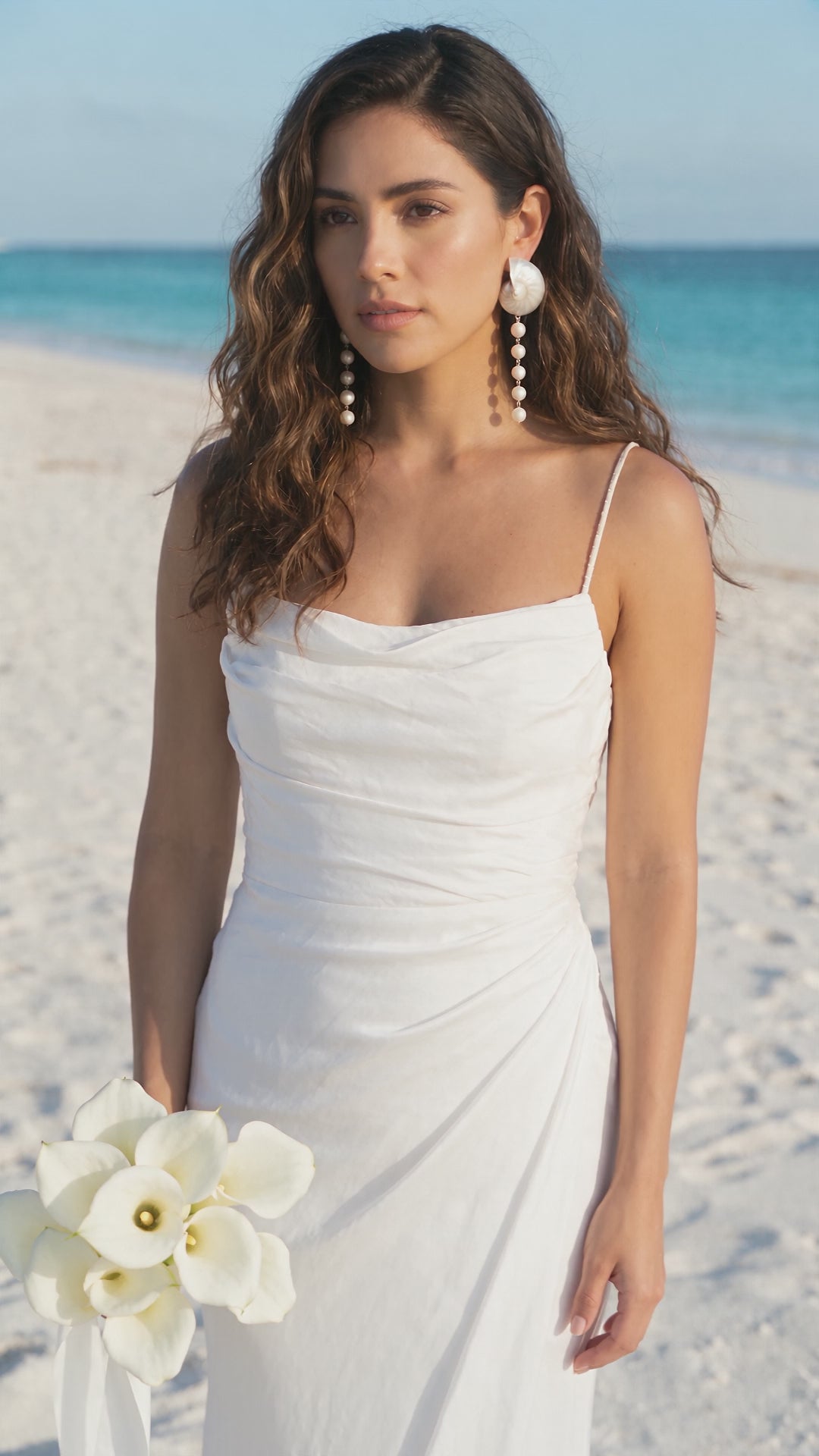 Video of a model wearing Large Pearl Nautilus Shell Cascade Earrings with a white dress and holding a white bouquet on the beach | Lily Frank Jewelry