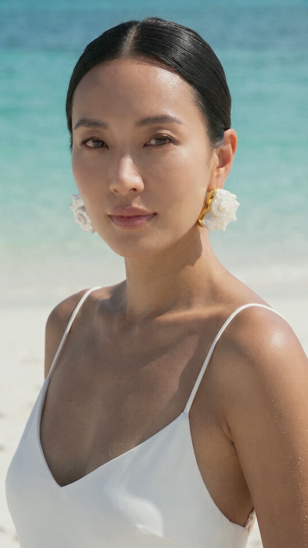 Model walking along a white-sand beach wearing Lily Frank Betsy Dolphin Shell Earrings in gold vermeil | Lily Frank Jewelry
