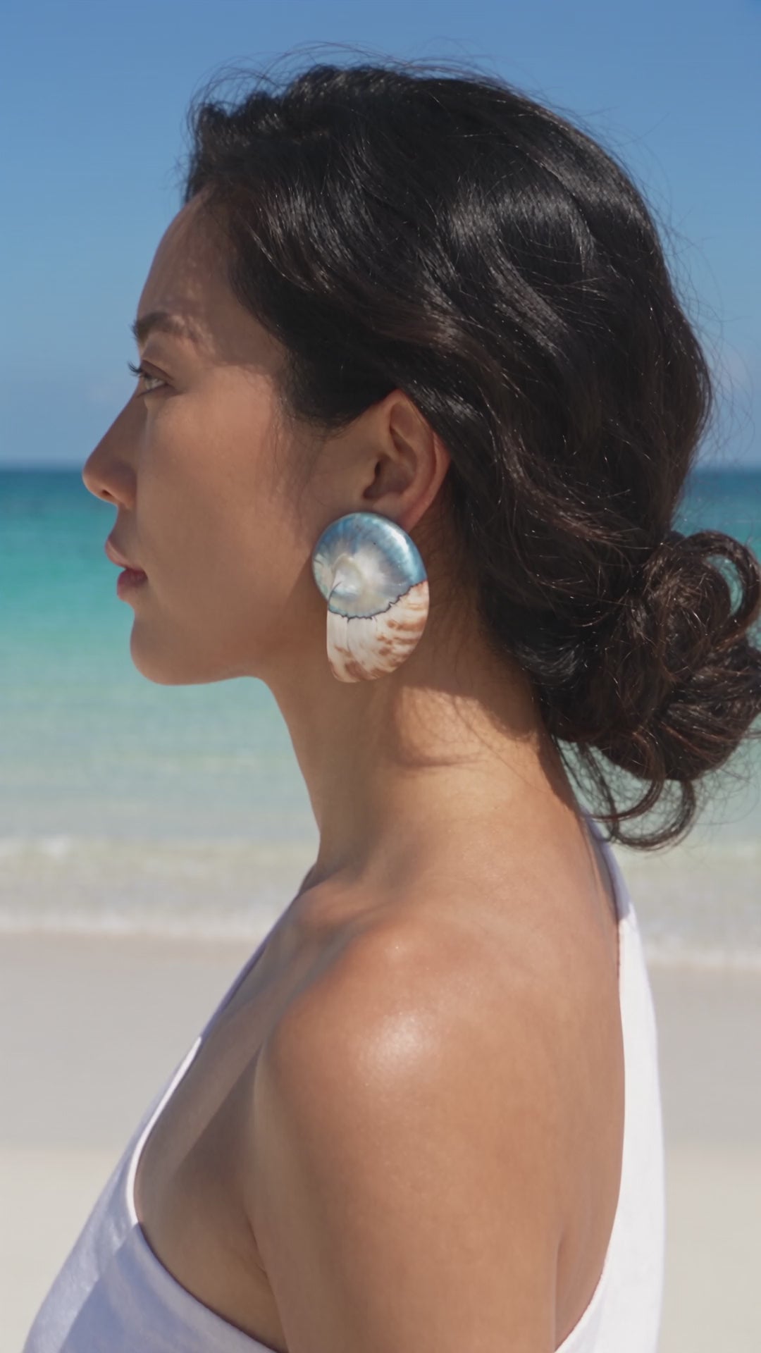 Video of a model wearing Oversized Banded Nautilus Shell Earrings in profile beside the ocean | Lily Frank Jewelry