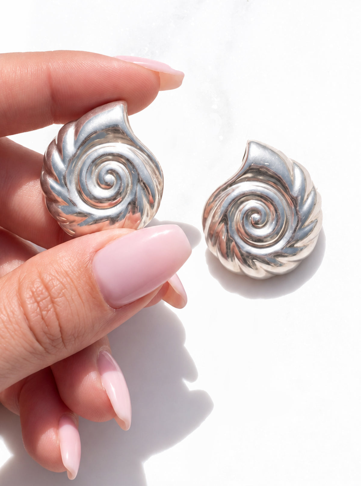 Vintage 925 Silver Nautilus Shell Earrings on a white background, with one earring held between fingers with a pale pink manicure | Lily Frank Jewelry