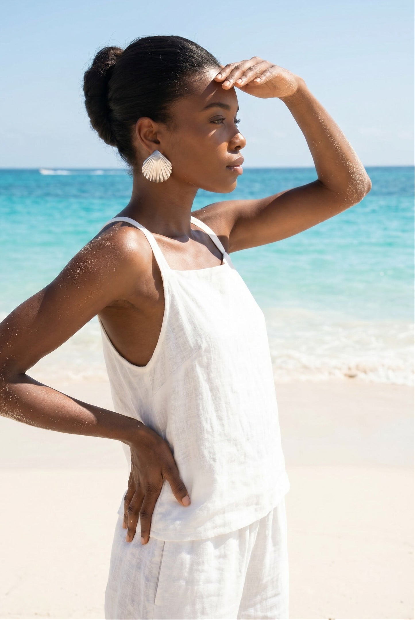 Woman in a white dress a pair vintage oversized 925 silver shell earrings standing on a beach with clear blue water and sky | Lily Frank Jewelry 