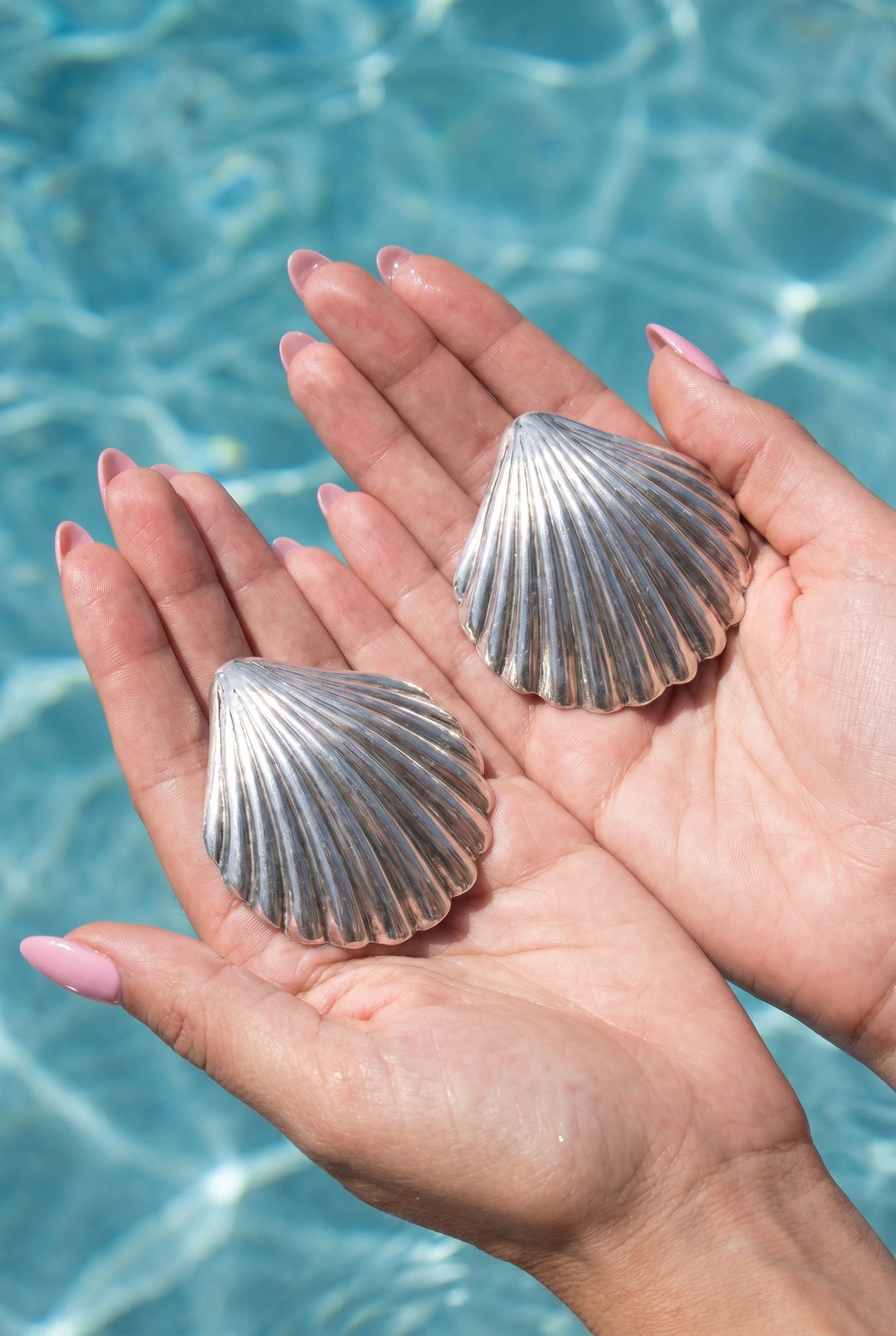 a pair vintage oversized 925 silver shell earrings held in hands against a blue water background | Lily Frank Jewelry 